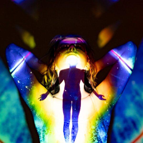 A silhouette emerges through colorful projections, evoking spirituality and energy.